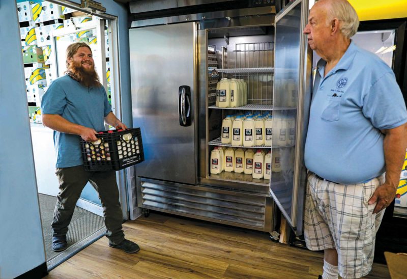 McKee Jack (right) helps Bram Robertson of Contoocook Creamery fill up the Laconia food pantry’s new refrigerator with fresh milk. (Photo by Cheryl Senter.)