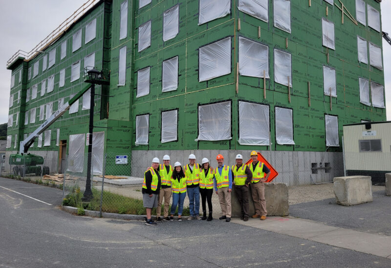Group of eight people with hard hats and safety vests in front of a building construction site